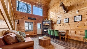 A cozy cabin interior with a fireplace, wooden walls, a sofa, and a dining area. - Heavenly Heights by Ghosal Luxury Lodging (Sevierville)