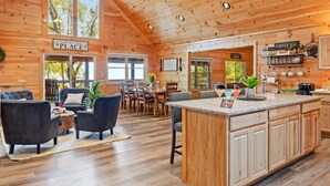 A spacious wooden cabin with a large dining area, a cozy seating area with dark chairs, and a kitchen with a coffee bar.