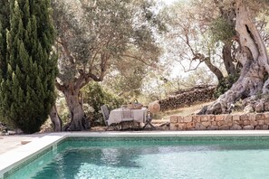 A pool area with a stone wall, a table with chairs, and a large tree. - SON BORRAS (Alaró)