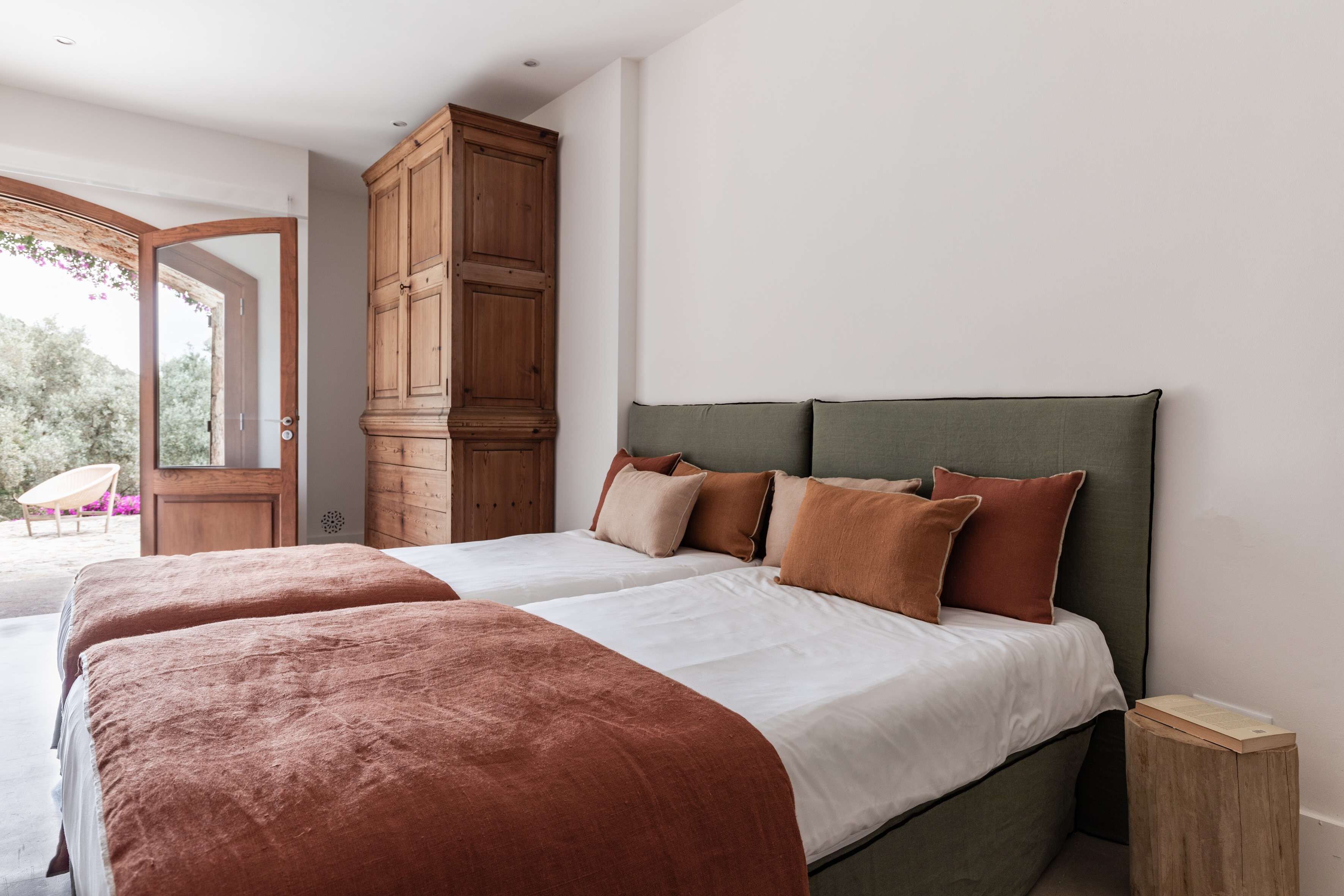 A bedroom with two beds, a wooden wardrobe, and a view through an open door.