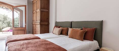 A bedroom with two beds, a wooden wardrobe, and a view through an open door.