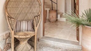 A wicker chair with a striped cushion, a potted plant, and an arched doorway leading to a staircase. - SON BORRAS (Alaró)