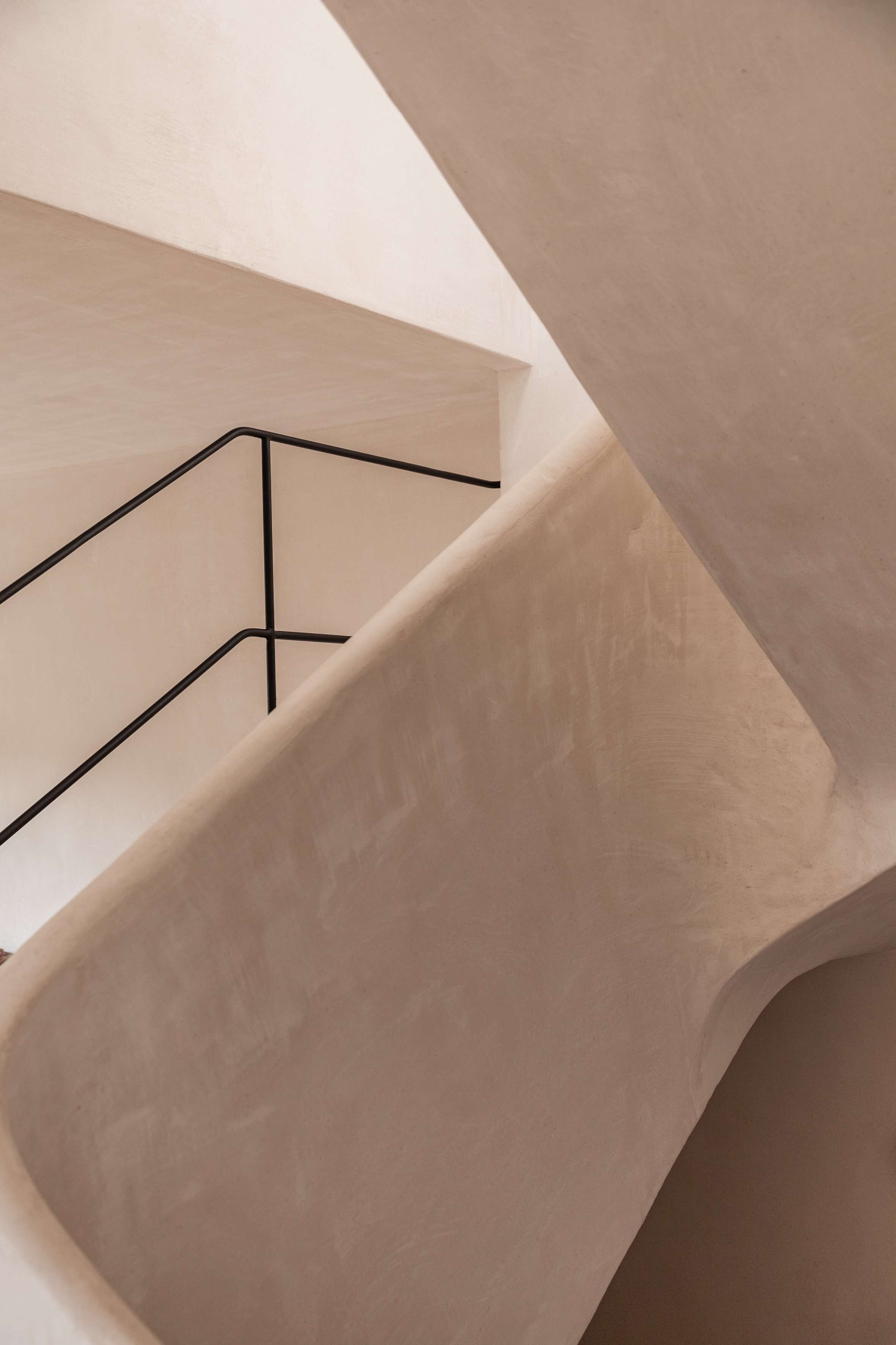 A modern staircase with a minimalist design, featuring a geometric metal railing and smooth, curved walls.