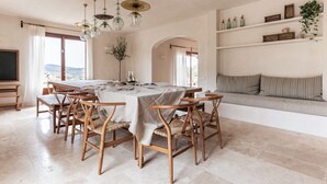 A spacious dining area with a long table and wooden chairs, a sofa with striped cushions, and a shelf with decorative items. - SON BORRAS (Alaró)