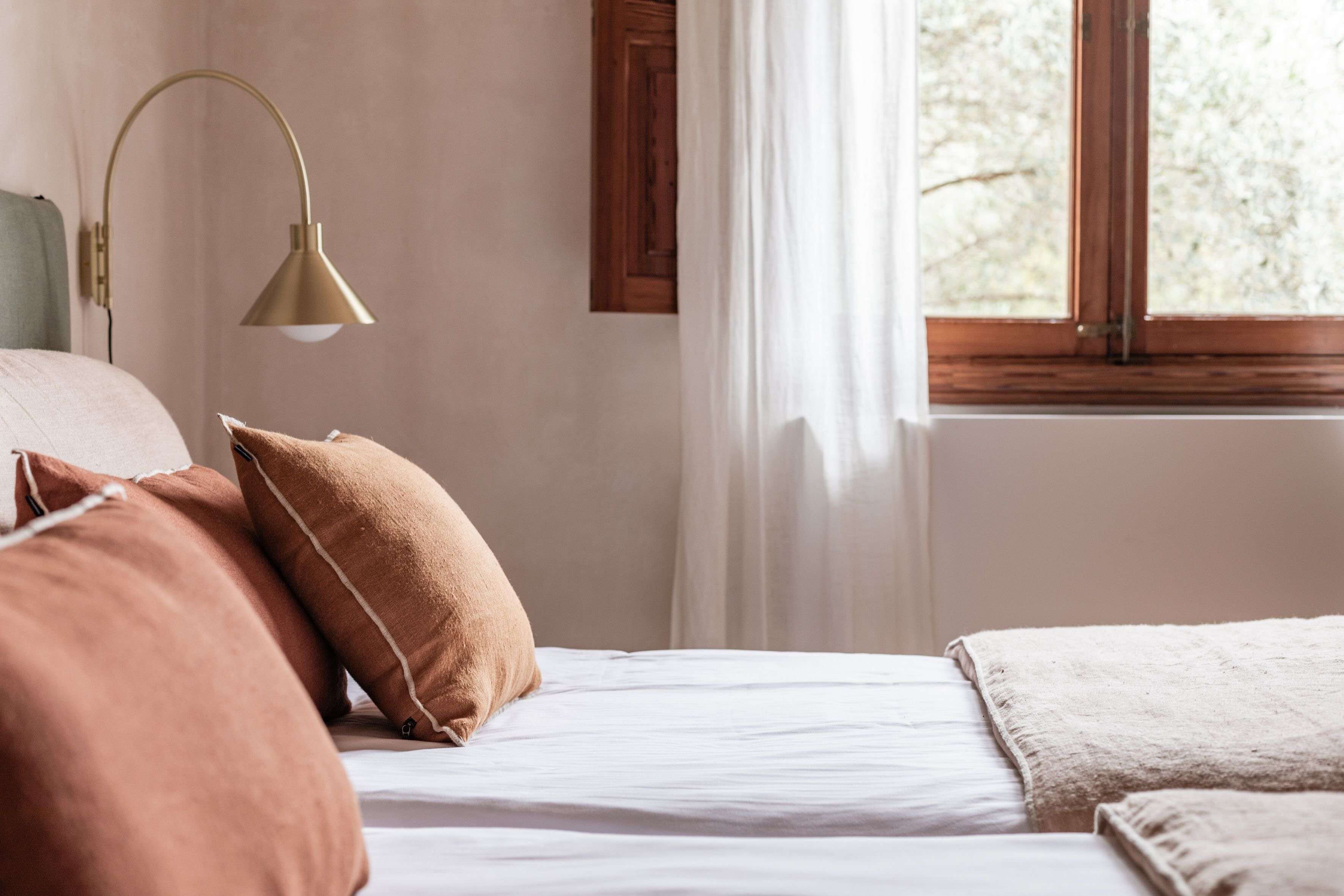 A bedroom with a bed, pillows, a lamp, and a window with curtains.
