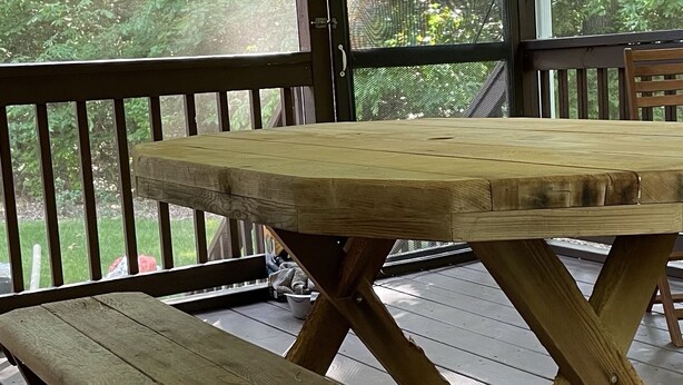 Une terrasse en bois avec une table et des bancs, entourée d’une rambarde et d’un treillis.