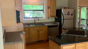 Une cuisine avec des armoires en bois, un comptoir en granit, un évier en acier inoxydable et un réfrigérateur.