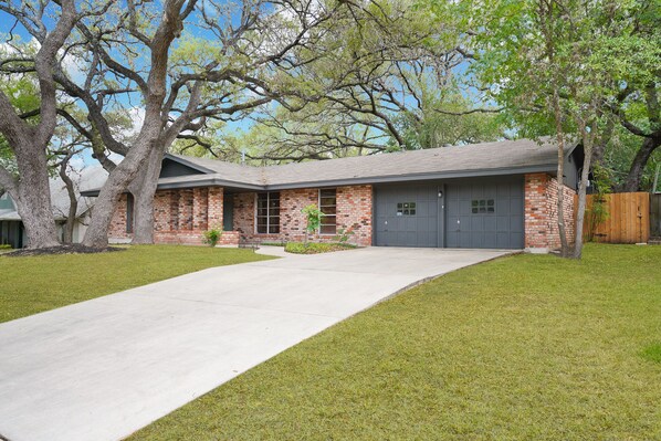 A two-story brick house with a grey garage door, a concrete driveway, and a well-maintained lawn.