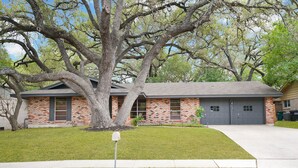 A two-story brick house with a large tree in front, a garage, and a well-maintained lawn.
