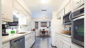 A modern kitchen with white cabinetry, stainless steel appliances, and a wooden floor.