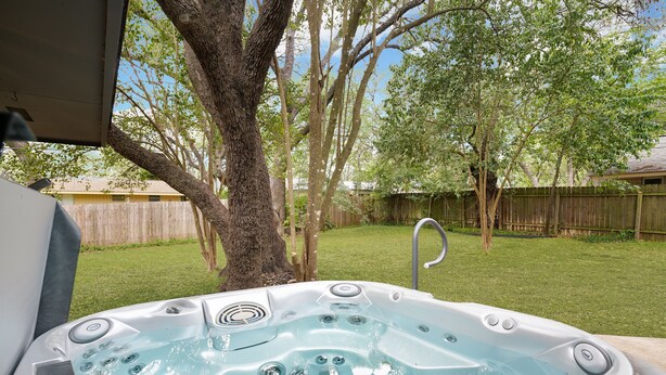 A hot tub in a backyard with a wooden fence and trees.