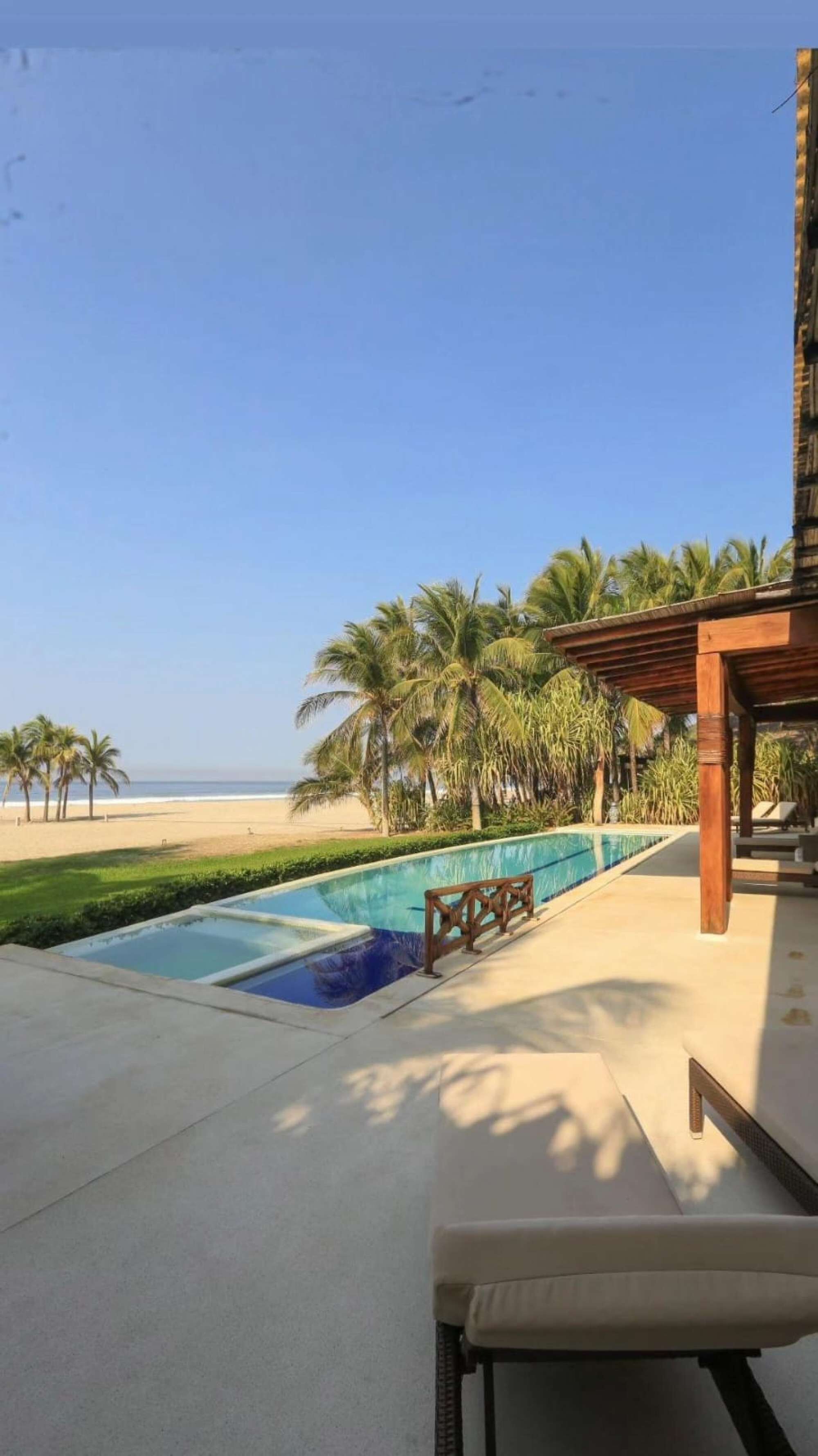A pool area with a view of the beach and palm trees.