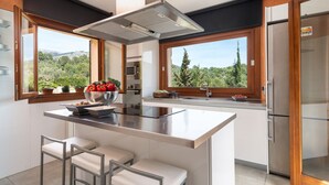 Uma cozinha moderna com uma ilha central, banquetas, forno embutido e grandes janelas com vista para o exterior.
