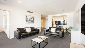 Una sala de estar moderna con dos sofás de cuero negro, una mesa de centro y una cocina visible a través de una puerta abierta.