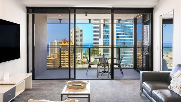 Un salón moderno con un amplio ventanal corredera que da a un balcón con vistas a la ciudad.