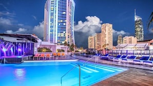 Una piscina con sillas de descanso y un horizonte urbano al fondo.