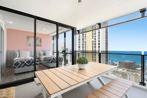 Enjoy the city view from this balcony with a table and potted plant, overlooking the ocean and high-rise buildings.