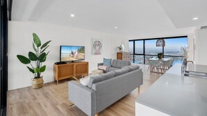 Una sala de estar moderna con un sofá gris, un mueble de madera y un televisor. Hay un ventanal con vistas a la ciudad.