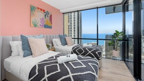 Un dormitorio moderno con dos camas, un ventanal con vistas a la ciudad y un cuadro abstracto y colorido en la pared.