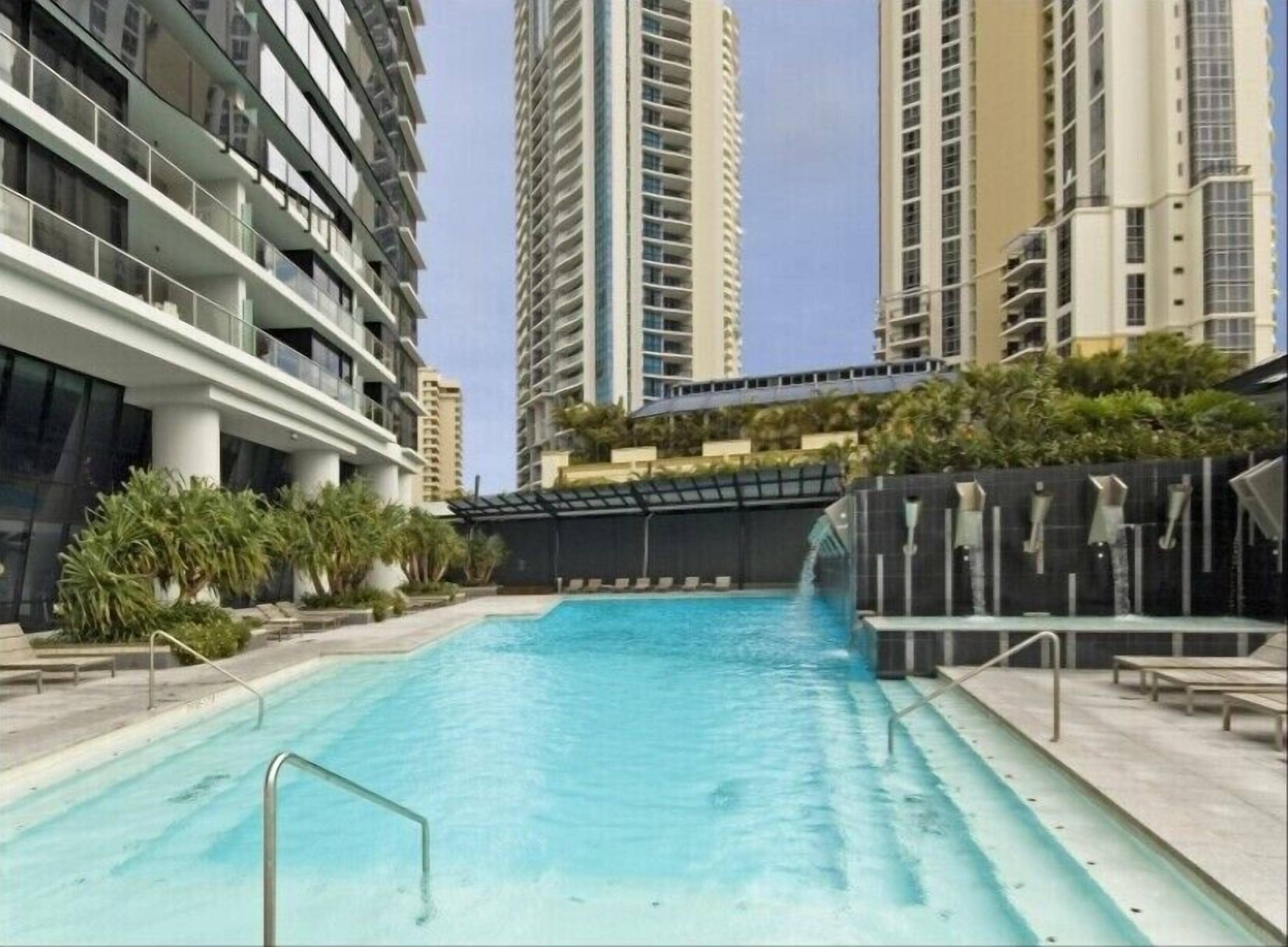 A swimming pool surrounded by high-rise residential buildings, with a covered area and lounge chairs.