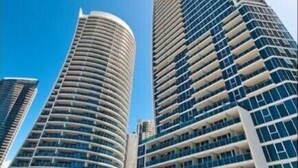 A modern high-rise hotel with a curved facade, a rooftop pool, and a clear blue sky. - 26 levels above Hilton hotel - 2 bedrooms (Surfers Paradise)