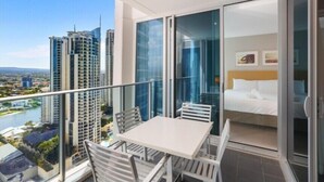 A balcony with a table and chairs, a bed, and a view of a river and buildings. - 26 levels above Hilton hotel - 2 bedrooms (Surfers Paradise)
