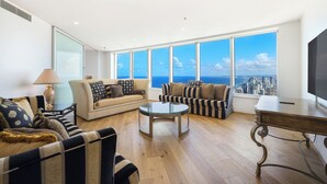 A modern living room with a large window offering a city view, a round coffee table, and two sofas with striped and patterned upholstery. - Sub Penthouse 6203 - 3 bedrooms Level 62 (Gold Coast)