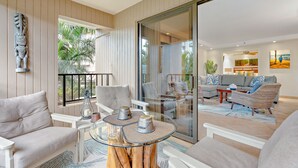 A modern living room with a glass partition, a sofa set, a coffee table with decorative items, and a view of the outdoor area.