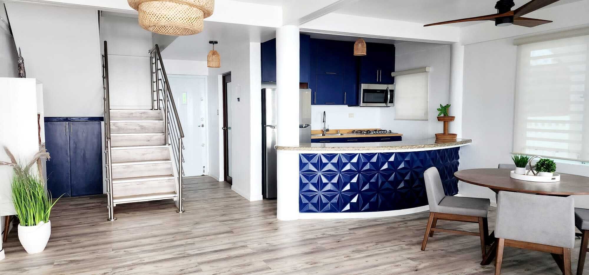 A modern kitchen with blue cabinetry, a central island, and a dining area with a round table and chairs.