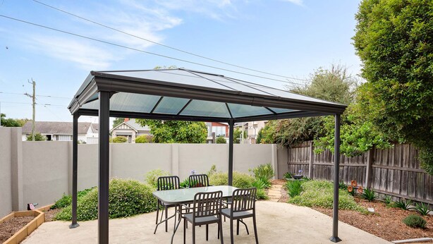 A covered patio area with a table and chairs, surrounded by a fence and greenery. - Lilly Pilly Pet Friendly Retreat in Essendon (Essendon)