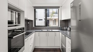 A modern kitchen with white cabinetry, a built-in oven, a microwave, a stainless steel refrigerator, and a window with a view of a building outside. - Lilly Pilly Pet Friendly Retreat in Essendon (Essendon)