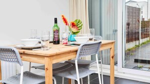 Un coin repas avec une table en bois, des chaises en métal et une fenêtre donnant sur un quartier résidentiel.