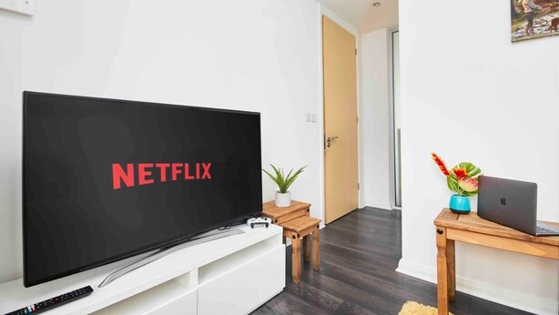 Un salon moderne avec un grand téléviseur à écran plat affichant le logo de Netflix, une table basse en bois, un ordinateur portable et une plante en pot.