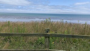 A coastal view with a wooden fence in the foreground, a grassy area, and the sea in the background. - One bedroom barn with free parking (Driffield)