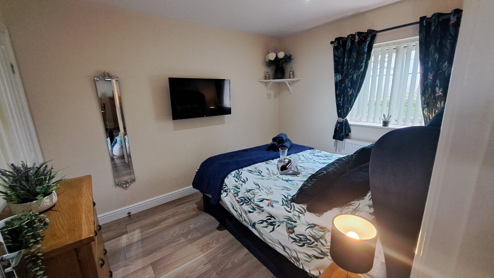 A bedroom with a bed, a TV, a window with curtains, a bedside table, and a lamp.