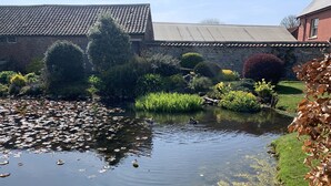 A pond with ducks, surrounded by greenery and a stone building. - One bedroom barn with free parking (Driffield)