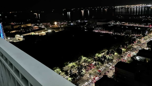 A nighttime view of a cityscape with a large body of water, illuminated buildings, and a busy waterfront area. - Cozy Urban Apartment in Pasay City (Pasay City)