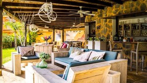 An outdoor seating area with wooden furniture, a bar with shelves of bottles, and a stone wall backdrop. - Apartment Aloha Hill Club Marbella (Marbella)