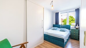 Un dormitorio con una cama, una silla verde, un aparador y una ventana con cortinas.