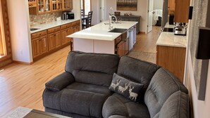 Una sala de estar moderna con un sofá seccional gris, una mesita de centro pequeña y una zona de cocina con armarios de madera y encimera de mármol.