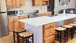 Una cocina moderna con armarios de madera, un refrigerador de acero inoxidable, un horno empotrado y una isla grande con taburetes de bar.