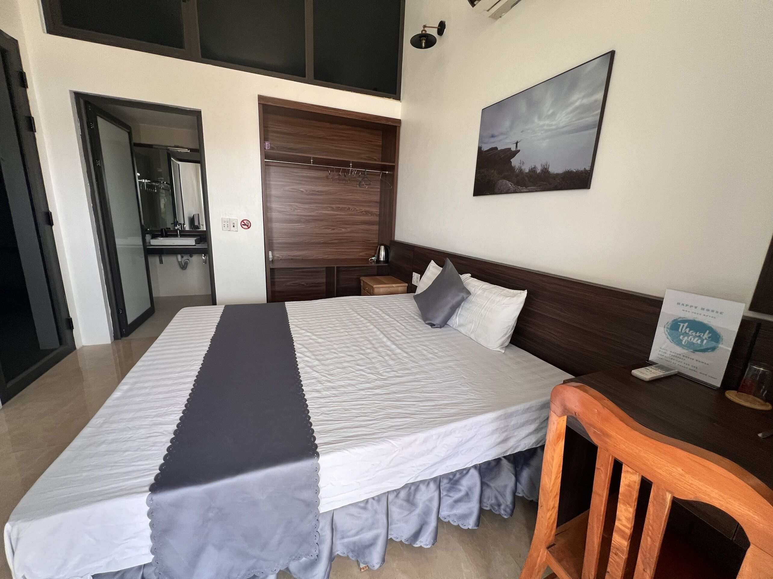 Habitación de hotel con una cama grande, cabecera de madera, un cuadro en la pared y un cartel en el escritorio.