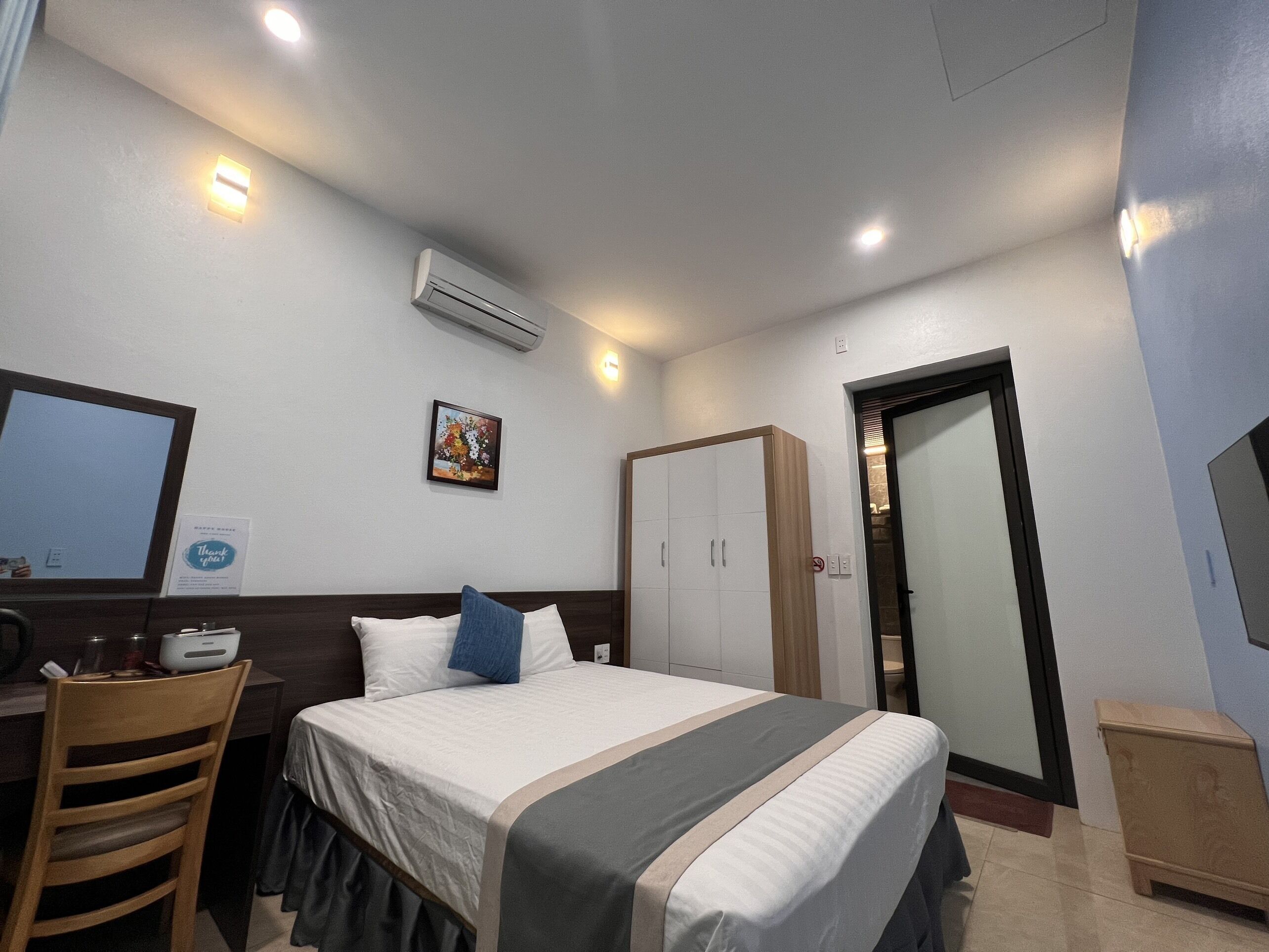 Una habitación de hotel con cama, escritorio, silla, aire acondicionado, armario y puerta.