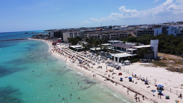 Un complejo turístico en la playa con varias edificaciones, una playa de arena y aguas turquesas cristalinas.