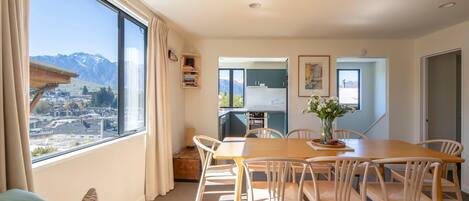 Un área de comedor con una mesa y sillas, vistas de la ciudad y las montañas a través de un ventanal grande, y una kitchenette al fondo.