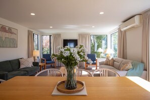 Un salon avec une table en bois, un canapé, un téléviseur et une fenêtre avec des rideaux.