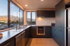 Una cocina moderna con lavavajillas, horno y electrodomésticos de acero inoxidable, ventanas amplias que ofrecen vistas a la montaña, y armarios oscuros.