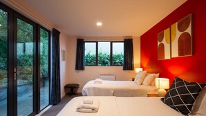 Een hotelkamer met twee bedden, een rode accentmuur en uitzicht op groen door grote ramen.