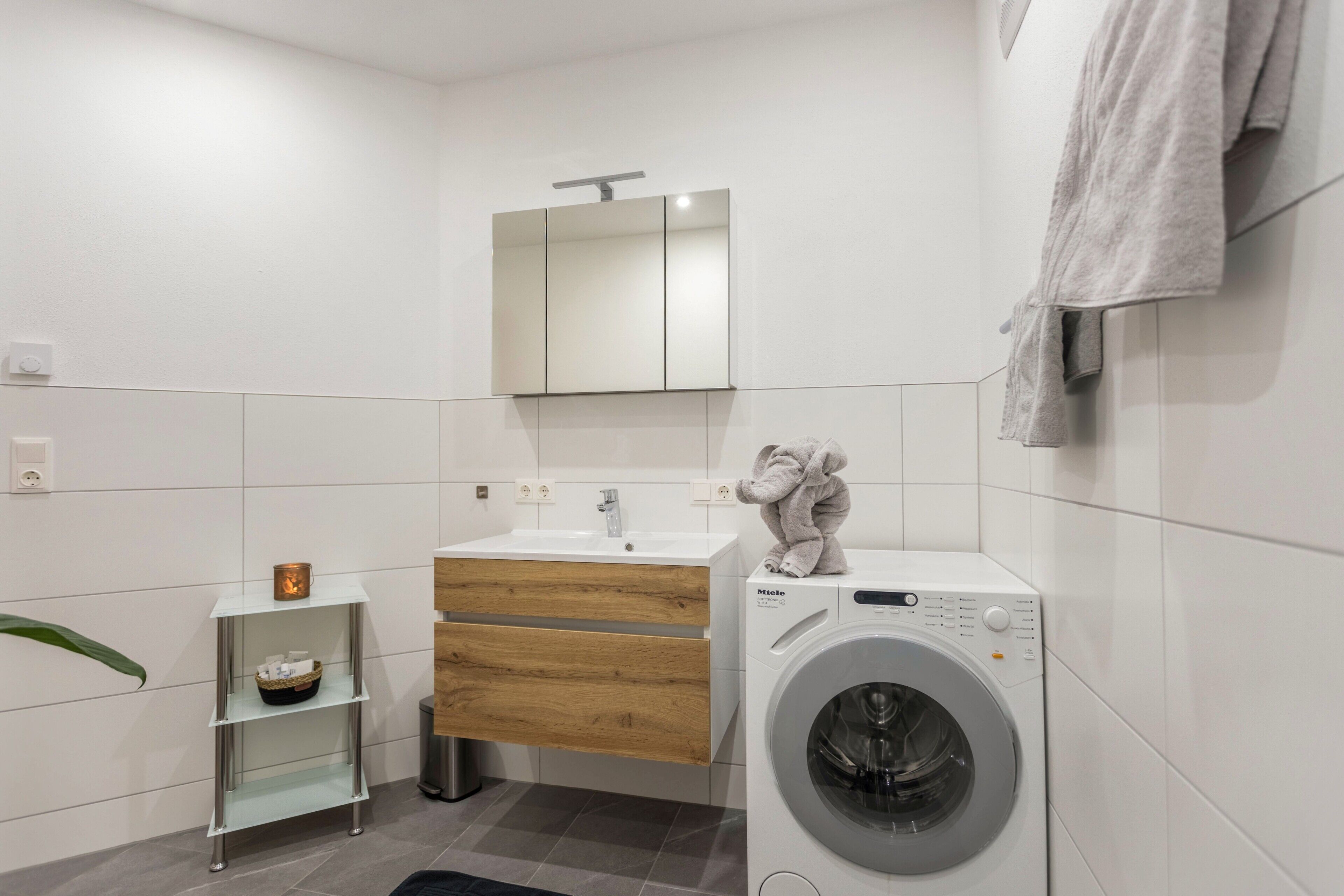 A modern bathroom with a washing machine, a mirror, a sink, and a towel rack.
