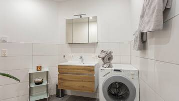 A modern bathroom with a washing machine, a mirror, a sink, and a towel rack.